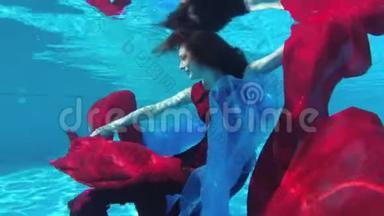 一个美丽的女孩穿着红裙子，手拿红蓝相间的布在水下游泳跳舞，看着镜头